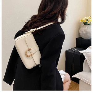 Close-up of cream crossbody bag with large gold horseshoe buckle on black blazer