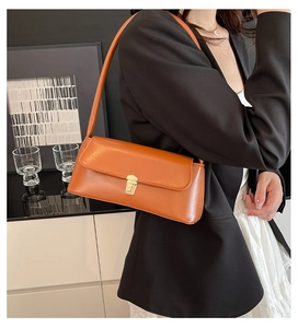 Detail of orange faux leather baguette bag with glossy finish and gold metal buckle lock
