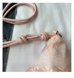 Detail of pink lace dumpling bag with satin texture and elegant knotted shoulder strap
