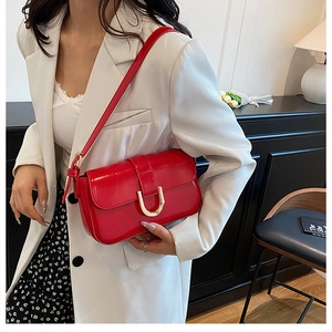 Detail of red glossy leather shoulder bag with a gold U-shaped metal buckle and flap