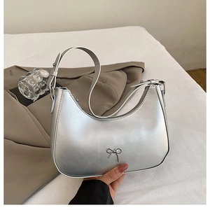 Detail of silver metallic crescent hobo bag featuring a decorative metal bow and strap