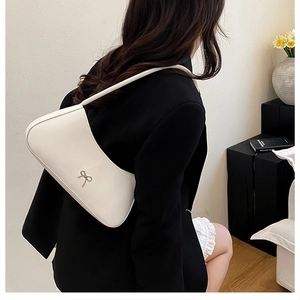 Minimalist white leather underarm bag with a silver bow detail shown on a model shoulder