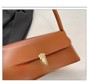 Detail shot of the golden rectangular hardware lock on a camel faux leather handbag