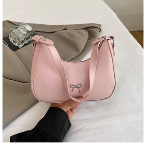 Detail of light pink crescent bag featuring a silver metal bow and wide shoulder strap
