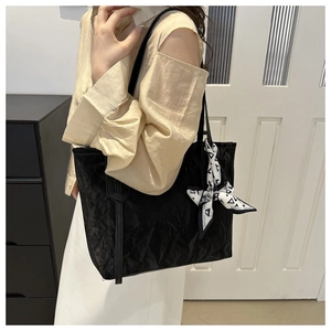 Detail of black tote bag featuring textured pleated fabric and decorative printed silk scarf