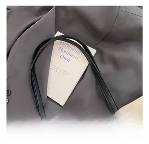Détail d'un cabas en toile avec bandoulière en cuir noir et boucle argentée sur veste