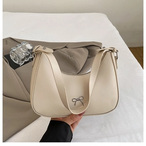 Detail of a creamy white half-moon shoulder bag with a delicate metal bow embellishment
