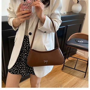Brown leather baguette shoulder bag with silver bow detail worn by a model in a white blazer