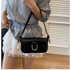 Detailed view of black patent leather shoulder bag with golden U-shaped buckle decoration