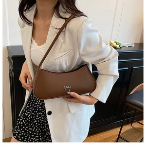 Brown leather underarm bag featuring a silver bow detail shown with a modern white blazer