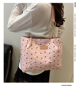 Detail of pink bucket bag featuring black bow patterns and elegant gold chain handles