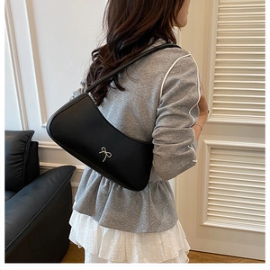Detail of minimalist black crescent shoulder bag featuring an elegant gold bow embellishment