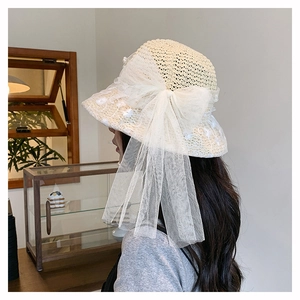 Detail of beige straw sun hat featuring a large white lace bow and pearl accents