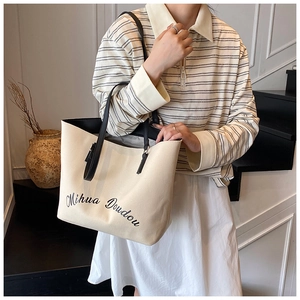 Détail du sac fourre-tout en toile blanc cassé avec texte et anses noires élégantes