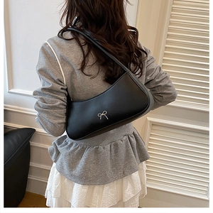 Close-up of black matte faux leather shoulder bag with a silver metal bow detail