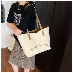 Detail of canvas tote bag showing brown leather straps and artistic lettering on beige fabric