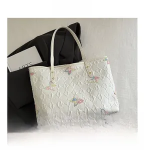 Dettaglio borsa shopper bianca con texture increspata, ricamo a farfalla e borchie oro
