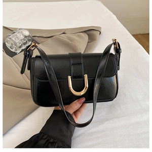 Detail of glossy black shoulder bag featuring a prominent gold U-shaped metal buckle