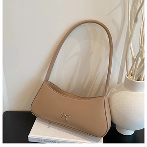 Detail of minimalist beige leather baguette bag with silver bow accent on white books