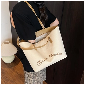 Close-up of the beige canvas tote bag with brown straps worn by a model in a room