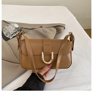 Detail of brown leather handbag featuring a signature gold U-shaped metal buckle closure