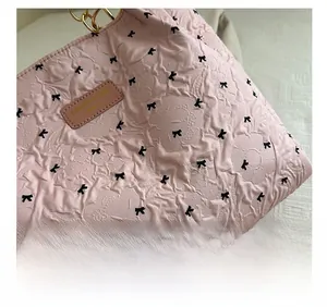 Détail du sac plissé rose avec imprimés nœuds, étiquette en cuir et poignée chaîne