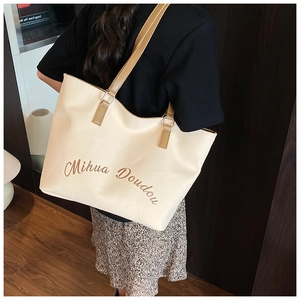 Close-up of cream canvas tote bag with brown leather handles and brand logo detail