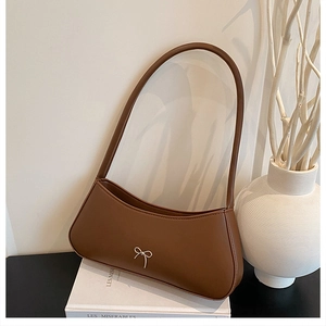 Close-up of brown crescent underarm bag with a silver metal bow on smooth leather