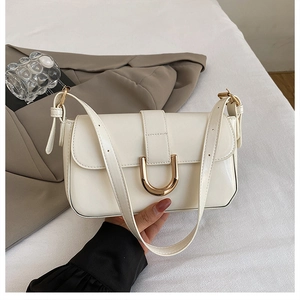 Detail of cream white faux leather shoulder bag with golden horseshoe buckle accent