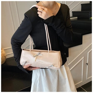 Detail of cream rectangular underarm bag featuring three silver metal bows and slim straps