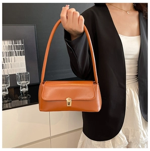 Brown faux leather baguette bag with a gold lock worn over a shoulder with a black blazer