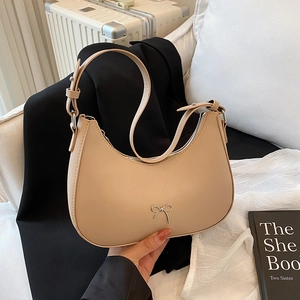 Chic beige crescent shoulder bag with metallic bow detail and adjustable leather strap