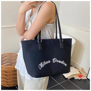Detail of black canvas tote bag featuring white Mihua Doudou embroidery text