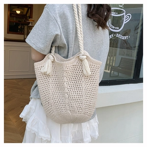 Close-up of beige crochet tote bag with thick rope handles and tassel details for vacations