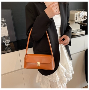Close-up of caramel leather baguette bag with gold metal square buckle in a cafe setting