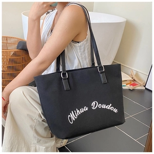Detailed view of large black canvas tote bag with white artistic lettering and gold buckles