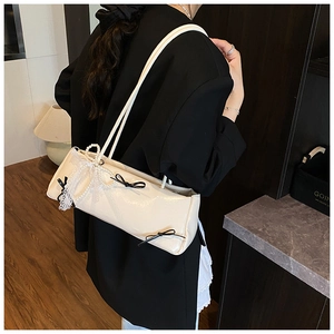 Detailed view of cream baguette bag with black bows and pearl lace charm on shoulder