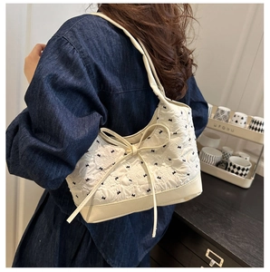 Detail of white quilted underarm bag with bow embroidery and knot design on blue denim