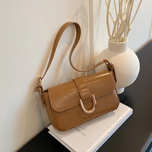 Brown glossy leather shoulder bag with gold horseshoe buckle on white book display