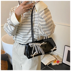 Close-up of black patent leather underarm bag with white lace bow and pearl charms