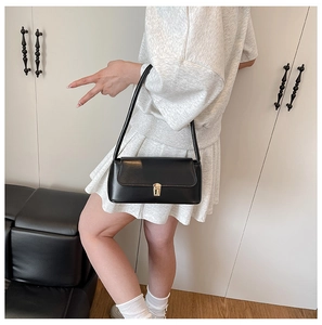 Detail view of the black retro baguette bag with gold buckle worn on a shoulder