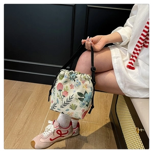 Close-up of floral embroidery on a cream canvas bucket bag with adjustable strap