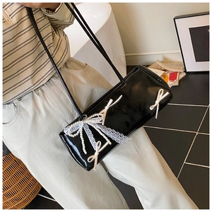 Close-up of black patent leather baguette bag with lace bows and pearl details