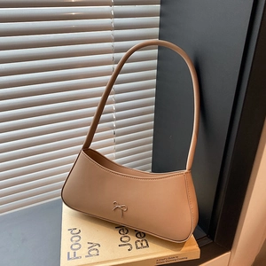 Minimalist beige crescent armpit bag with silver bow accent on vintage book