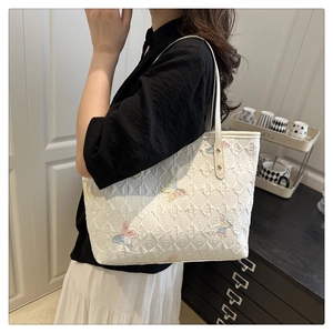 Detail of white tote bag featuring colorful butterfly embroidery and logo print