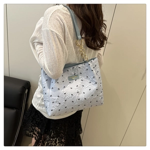 Détail du sac cabas bleu clair avec motifs nœuds noirs et chaîne dorée chic