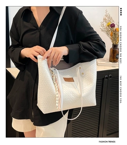 Close-up of white woven tote bag featuring a leather logo patch and long shoulder straps