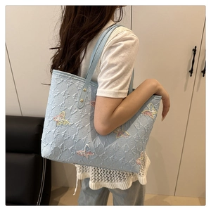 Dettaglio borsa tote azzurra con motivo E a rilievo e ricamo di farfalla multicolore