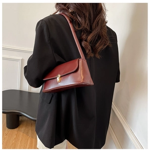 Detail of burgundy baguette bag with gold lock buckle on a black blazer outfit