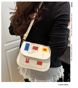 Detail of white PU leather crossbody bag featuring vintage cartoon stamp patches and gold buckle